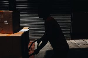 A silhouette of a person pushing a cart with cardboard boxes