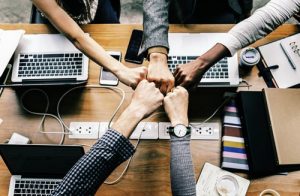 Delegating office moving taksts requires teamwork exemplified by five people fist bumping each other over a table.