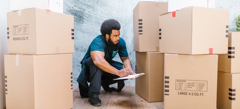 man standing among moving boxes and writing notes