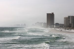 A hurricane hitting a coastal city, the sea is restless, waves are hitting the shore hard and tall buildings are hard to see through the mist