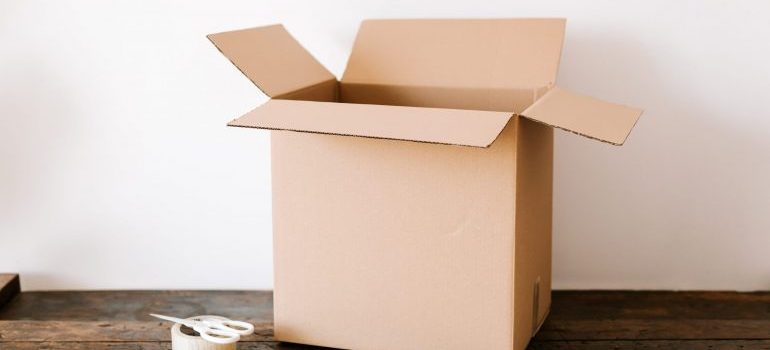 Cardboard box on dark wooden table near tape and scissors