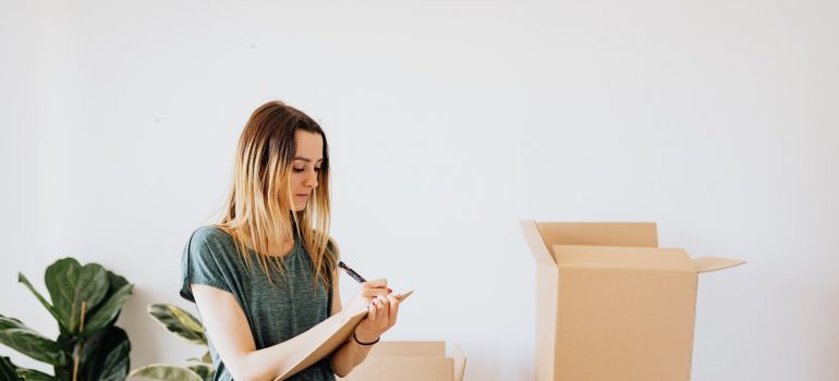 A woman making notes near cardboard boxes.