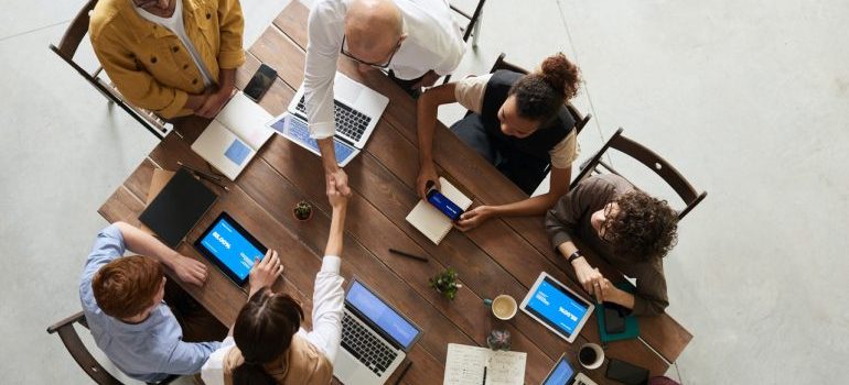 A meeting where office workers sit around a conference table with laptops and tablets, before choosing the best commercial movers Bradenton offers.