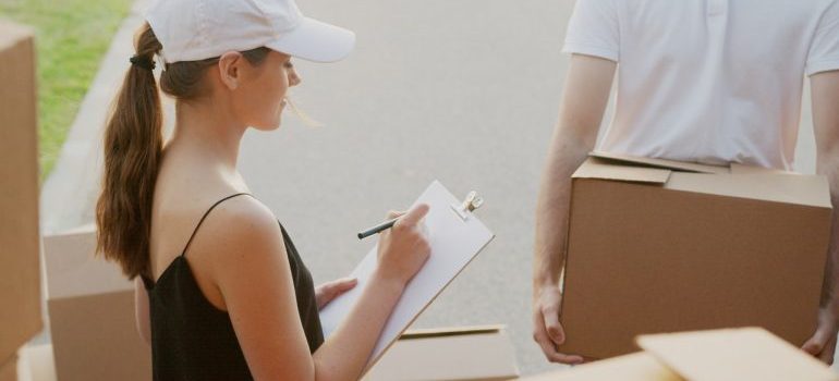 A woman with a clipboard and pen surrounded by cardboard boxes.