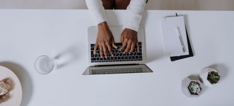 A person typing on a laptop on a white table.