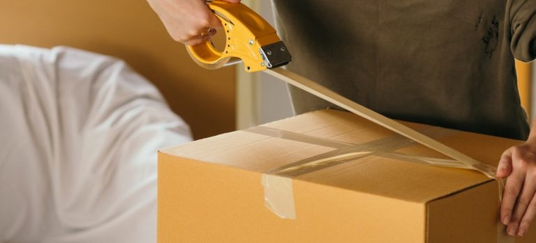 A man applying tape to a cardboard box, before hiring the best long distance movers in Miami Beach.