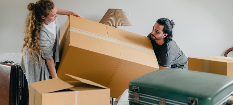 Two people carrying a huge cardboard box instead of hiring the best local movers in Hollywood.