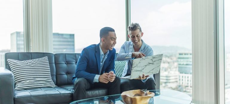 Young businessmen looking at laptop, excited to have found residential movers Hallandale Beach.