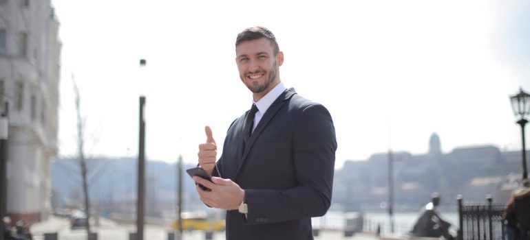 A smiling businessman holding a phone and giving thumbs up.