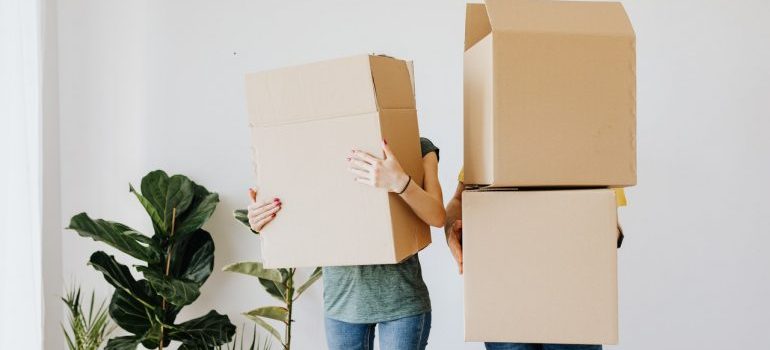 A couple holding large moving boxes.