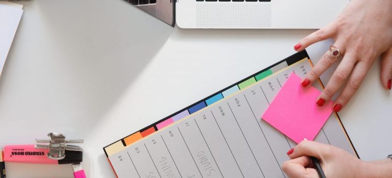 A woman's hand with pen and planner, and a sticker note