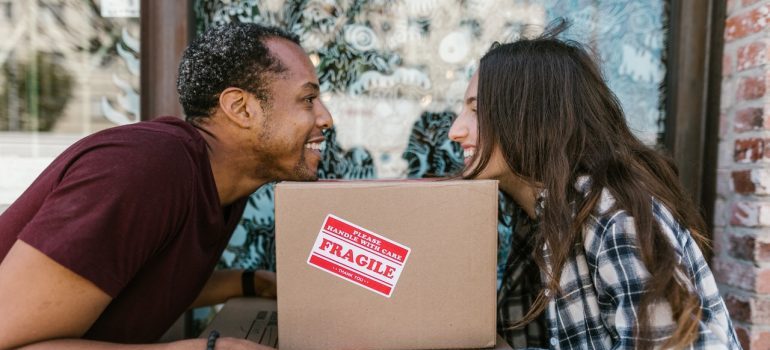 A young couple smiling while holding boxes.