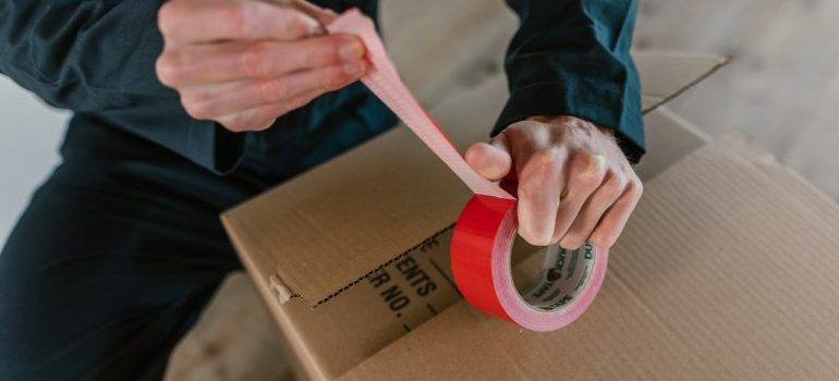 Packer sealing a cardboard box with a tape - residential movers West Palm Beach