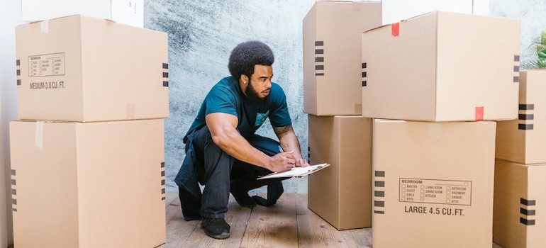 man writing on a clipboard surrounded by boxes is one of commercial movers Fort Lauderdale