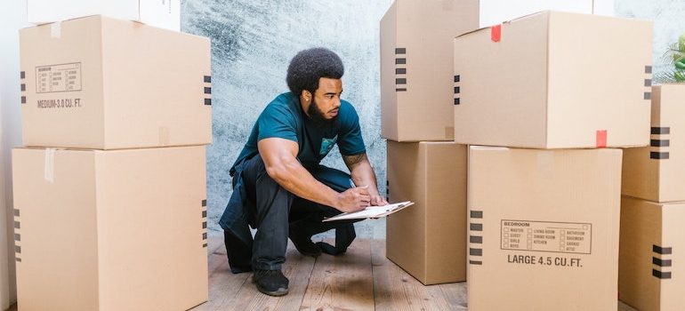 Man writing on a clipboard surrounded by boxes is a part of best movers Bradenton Beach