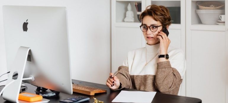  a woman sitting in front of the computer and making a phone call trying to find the best Melbourne FL long distance movers