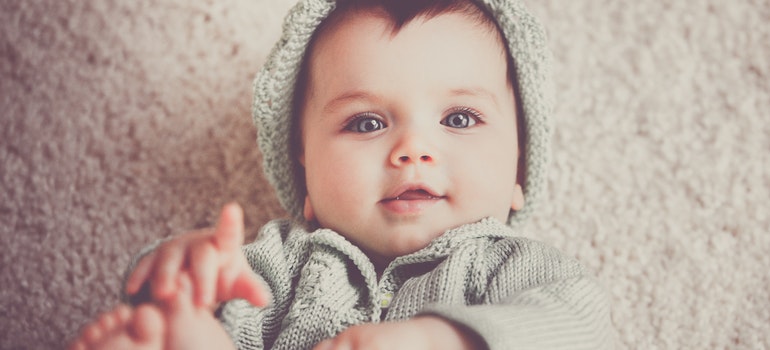 A baby is iyling on the floor and looking at the camera.