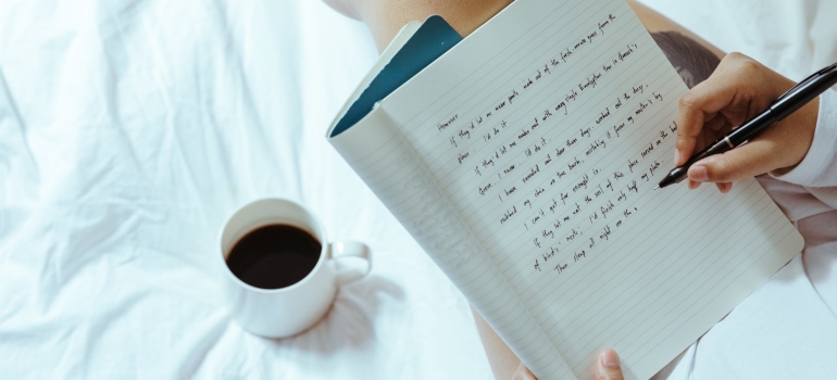 A woman writing a plan in a notebook with a cup of coffee