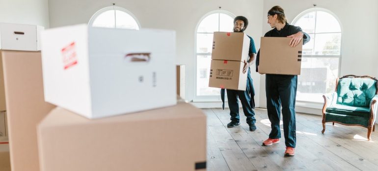 two moving crew personnel carrying cardboard boxes across the room