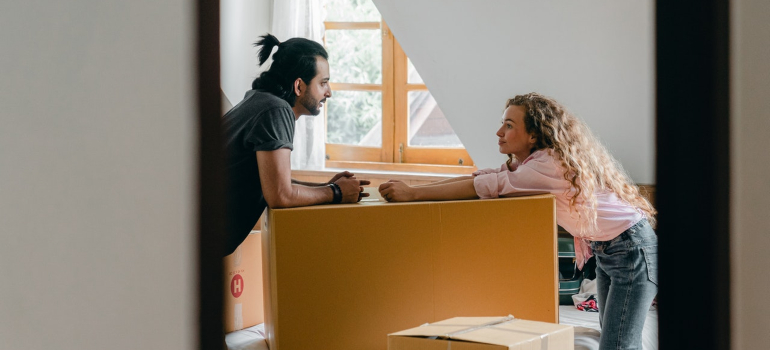 a couple resting over a large cardboard box in their bedroom