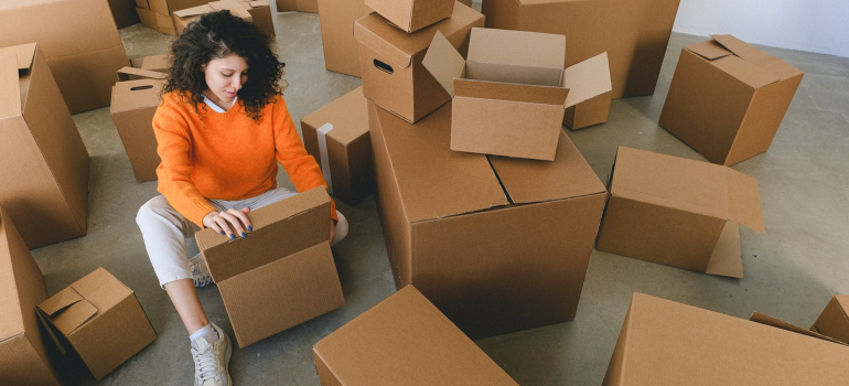 a young woman in an orange sweater sitting in between a large number of cardboard boxes