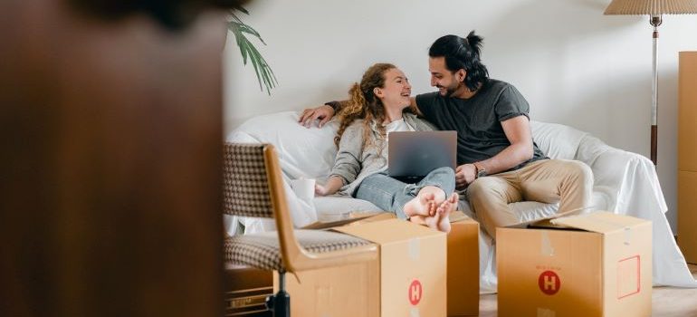 a couple searching for movers online, surrounded with moving boxes 