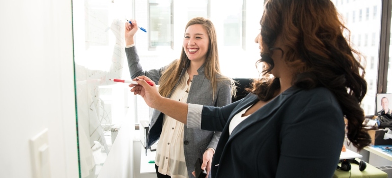 two business women writing a office moving checklist on a white board