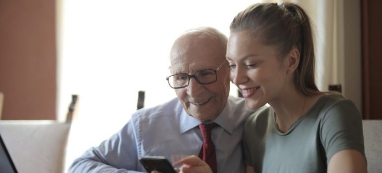 Girl and older man looking at the phone in front of laptop - connecting with local movers Palm city FL was never easier