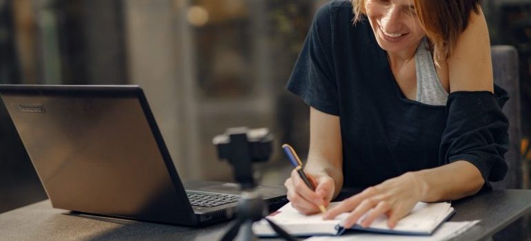 a woman writing something in her notebook by the laptop while searching for the best movers Palm City FL