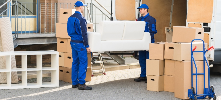 Full length of young male movers carrying sofa outside the truck on street.