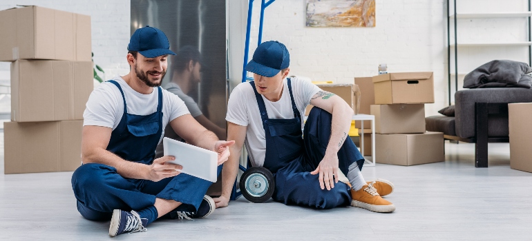 Two movers using a digital tablet while sitting on the floor.