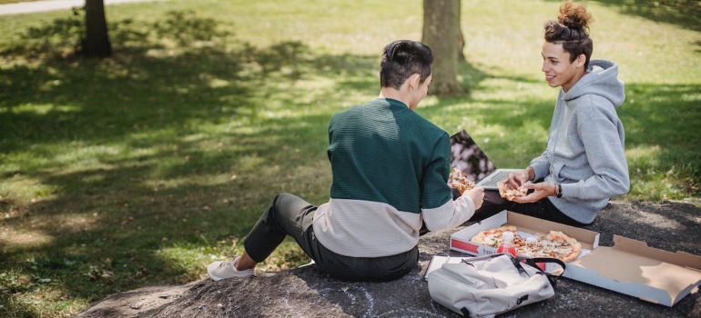 two men eating pizza in the park