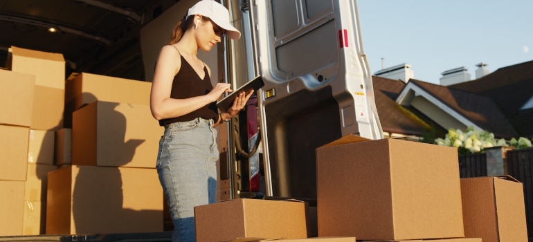 a woman consulting a list of items while counting boxes next to a van
