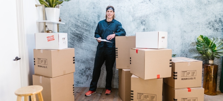 a man standing in-between cardboard boxes with a list to depict long distance movers Pine Hills FL and what they can do for the process