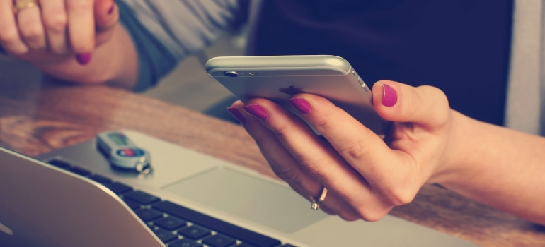 Woman holding a phone above lap top