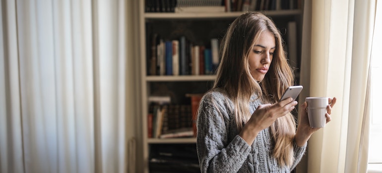 Young woman in gray sweater using her phone while standing