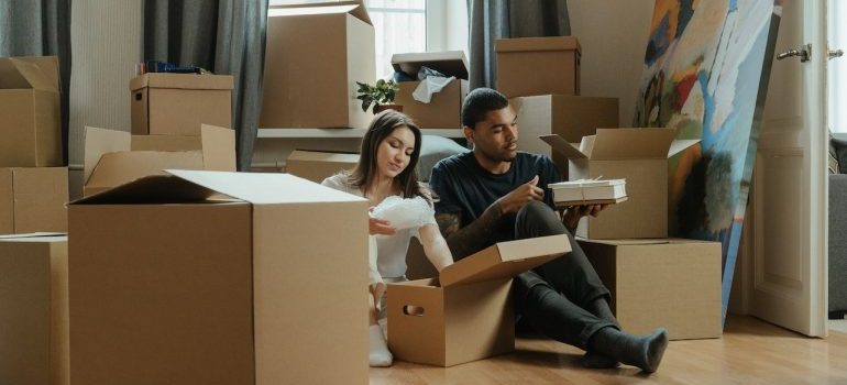 A couple sitting on the floor amongst boxes waiting for local movers Doral FL