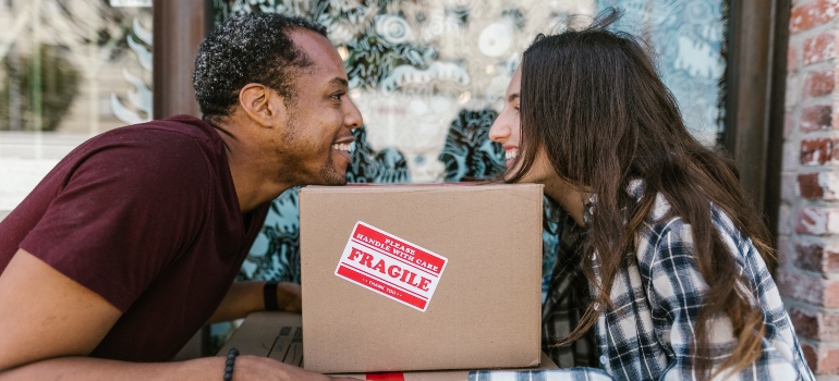 A man and a woman smiling to each other while leaning on a moving box