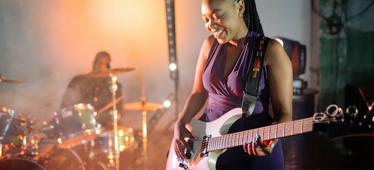 A person playing a guitar with a drummer in the back