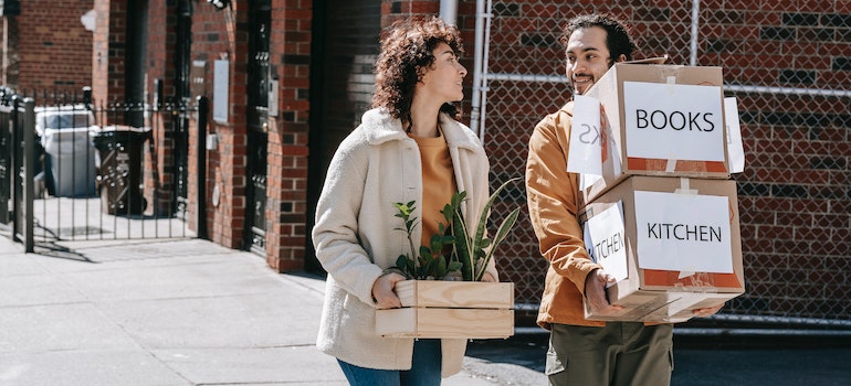 A man and a woman smiling in the street while carrying boxes