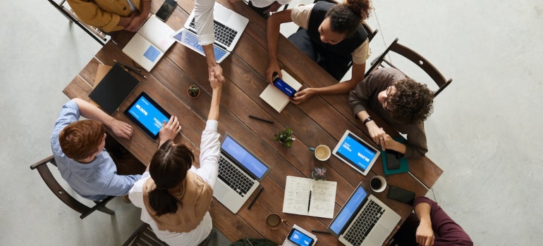 People shaking hands, using phones and laptops on a business meeting in an office