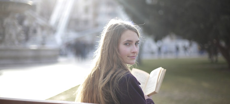 A woman sitting on a bench with a book in her hands turned around to look at the camera