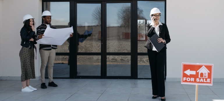 People standing in front of a house with a for sale sign