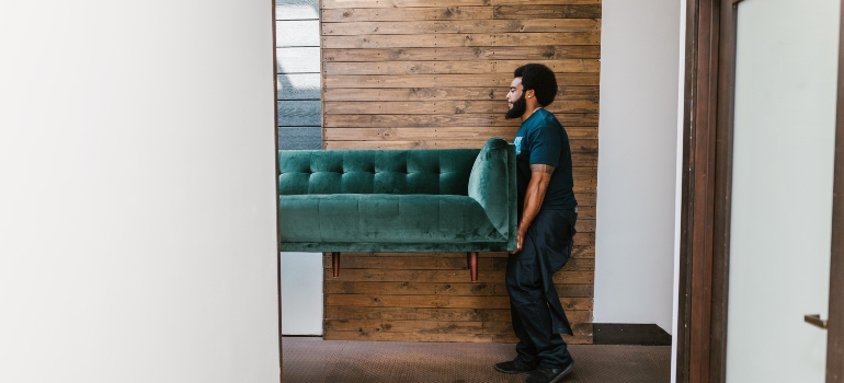 A moving company employee carrying a green velvet couch