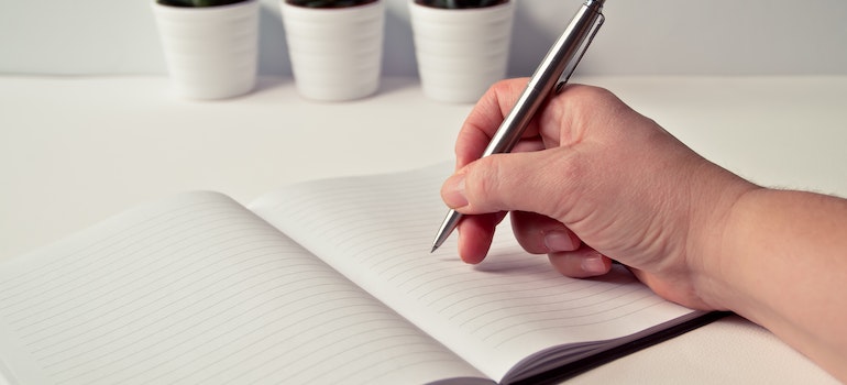 A person using a pen and a notebook to make the strategy for moving while sick.