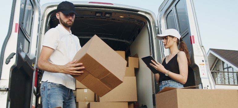 A man and a woman carrying moving boxes in front of a van