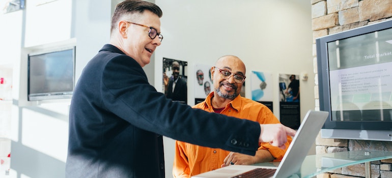 A man pointing at a computer while laughing with another man 