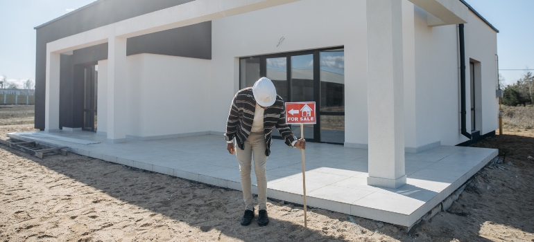 A man posting a For Sale sign in front of a house.