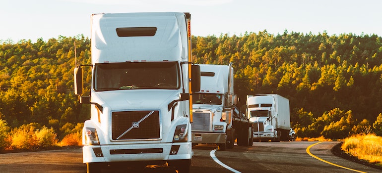 A moving truck with two more trucks behind it on a long road