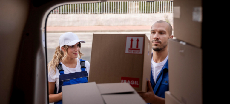 Two long distance movers Wesley CHapel taking cardboard boxes out of a moving van in blue overalls and white baseball cap